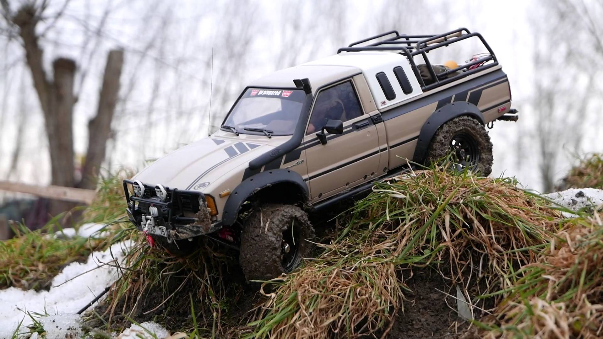 A scale RC truck driving over grass, mud, and snow